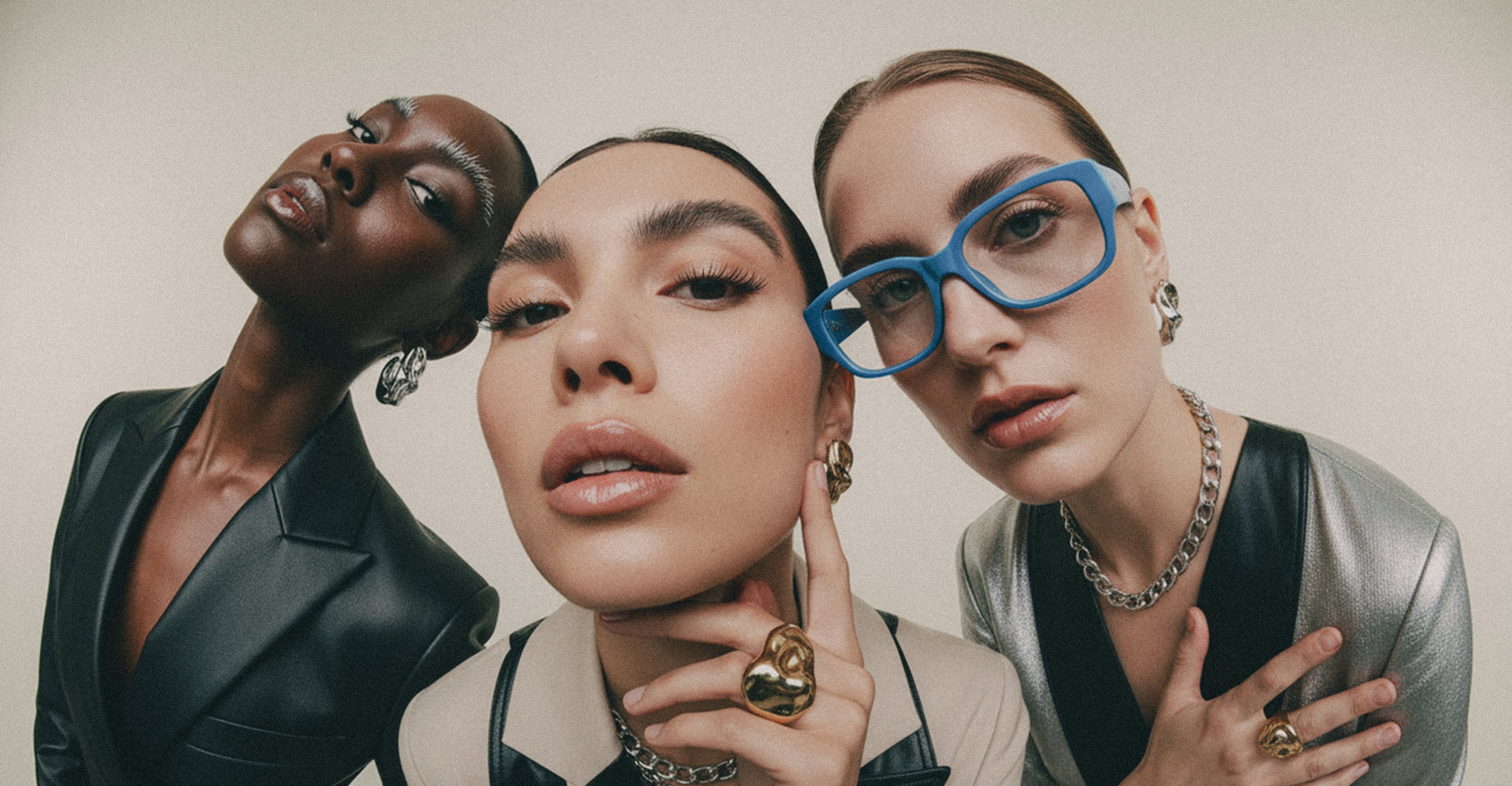 Three women posing together with stylish jewelry against a neutral background